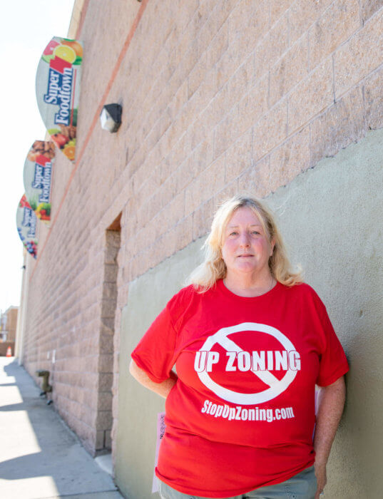 Carol Brumley-McManus wears a shirt with a red shirt wthat has an x over the word Upzoning and the website StopUpzoning.com next to the Super Foodtown on Bruckner Boulevard