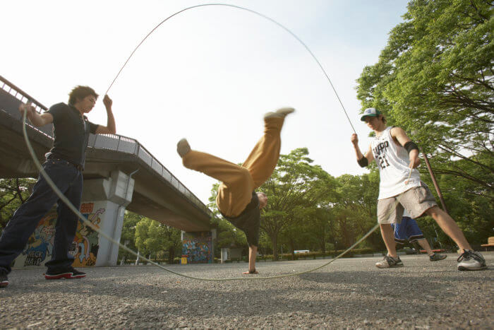 Three young men playing double dutch in a park.