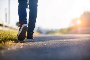 Close-up of legs walking at sunset on a paved path lined with grass on the left.
