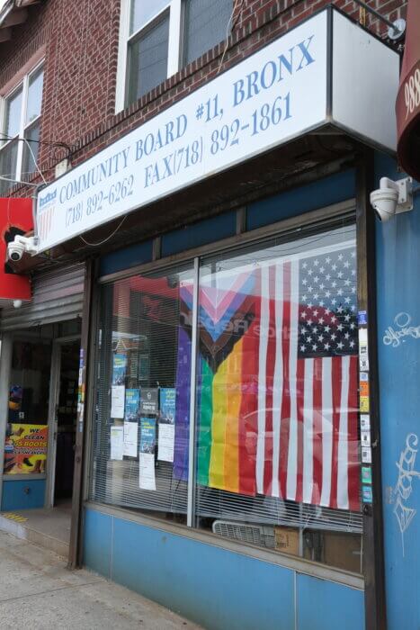 exterior of Community Board 11 office with inclusive pride flag and American flag hung up inside the window